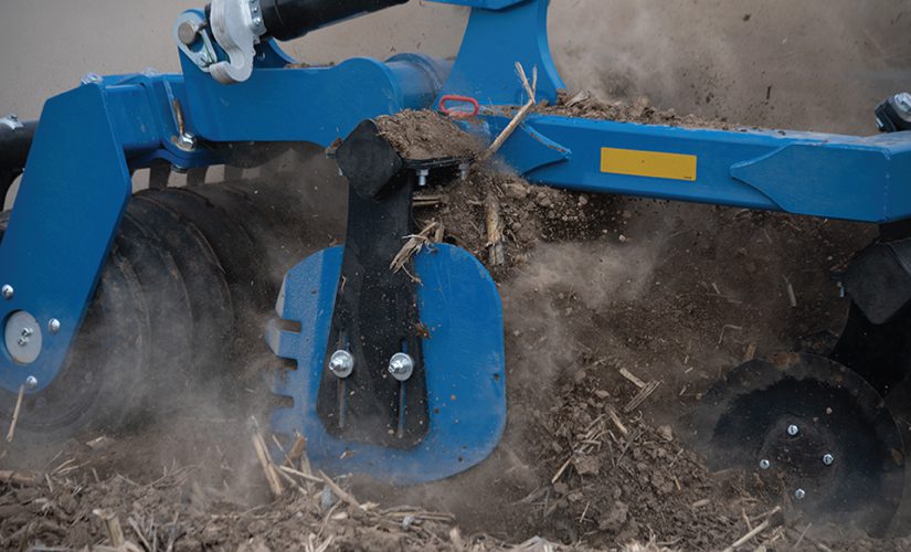 Mach Till tillage implement detail - close up of discs ripping soil with dirt deflector arm in the forefront